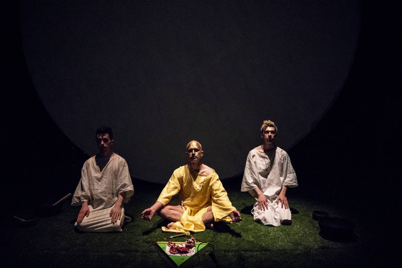 Three individuals sit like yogis behind a microphone and bowl of pomegranates